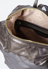 Bolso de mano marrón metálico con diseño acolchado, que cuenta con una cremallera dorada, un forro de tela beige con un sutil patrón de marca y un bolsillo interno con cremallera.