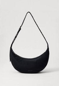 Melna pusmēness formas plecu soma ar regulējamu siksnu un rāvējslēdzēja aizdari, priekšpusē diskrēts "Michael Kors" logotips.