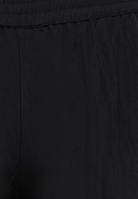 Gros plan sur un tissu noir avec une ceinture élastique, montrant la texture et les détails des coutures.