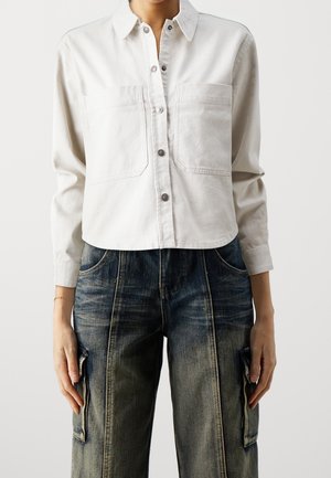 Vit kortärmad skjorta med krage, som har två framfickor och en slät yta, matchad med blå, slitna vida jeans.