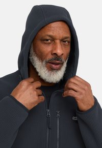Giacca in fleece a coste grigia scura con chiusura a zip e cappuccio, dotata di logo sul petto e foderata in fleece per calore.