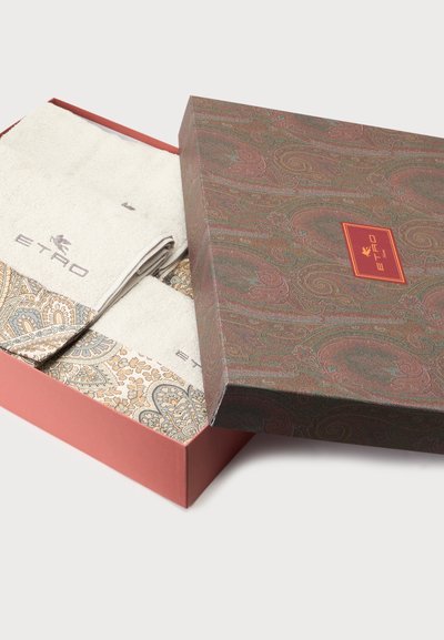 Deux serviettes beiges avec des bords à motifs et le logo ETRO à l’intérieur d’une boîte décorative partiellement ouverte avec un motif cachemire et une étiquette rouge.