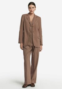 Brązowy lniany garnitur z dopasowaną marynarką i szerokimi spodniami. Posiada jedną kieszeń na piersi, dwie dolne kieszenie i detale z guzikami.