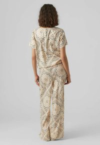 Kortärmad topp och vida byxor i ljusbeige med intrikata mörka mönster. Slät tygkänsla med avslappnad passform.