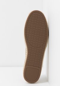 Semelle de chaussure en caoutchouc brun texturé avec un motif répétitif de logo "MK" et un grip rectangulaire au talon, sur fond blanc uni.