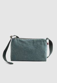 Borsa a tracolla rettangolare in denim blu con tracolla nera regolabile e chiusura con cerniera superiore su sfondo neutro.