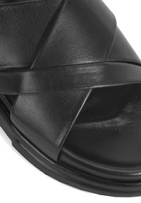 Zwarte leren sandaal met gekruiste riemen, een gladde textuur en een afgeronde zool. Minimalistisch ontwerp met stevige constructie.