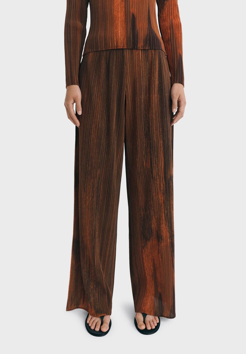 Bruine en oranje gestreepte broek in een losse pasvorm, met een hoge taille en brede pijpen, gedragen met een gestreept shirt met lange mouwen.