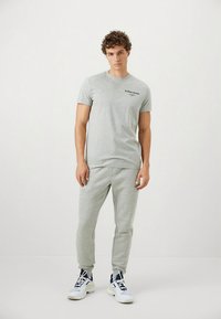Gray cotton short-sleeve t-shirt with a black logo, paired with matching gray sweatpants. Model wears white and navy athletic shoes.