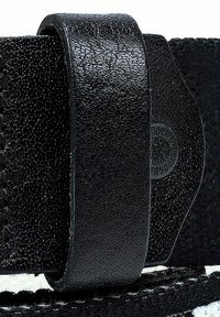 Sangle en cuir noir avec une surface texturée, présentant une boucle lisse et un détail circulaire en relief à une extrémité.
