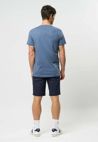 Niebieska bawełniana koszulka o luźnym kroju, zestawiona z granatowymi szortami. Białe skarpetki i casualowe buty dopełniają strój. Prosty, minimalistyczny design.