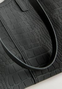 Sort faux læder tote taske med et tekstureret krokodillemønster, der har en glat overflade og runde håndtag.