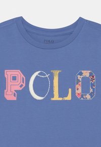T-shirt in cotone blu con la parola "POLO" in lettere multicolori: rosa, bianco, giallo e con un motivo floreale. Tessuto morbido con collo a giro.
