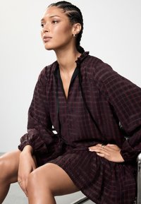 Tumepunase mustriga kleit volangikaeluse, pikkade volüümvarrukate ja musta äärisega. Sile tekstuur, lai lõige ning kihiline seeliku disain.