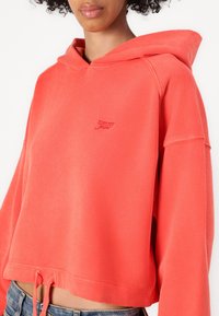 Sudadera coral recortada con dobladillo ajustable mediante cordón, con un pequeño logo bordado. Confeccionada en suave algodón con un corte relajado.
