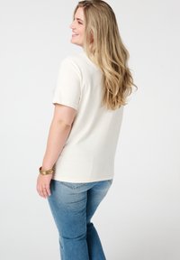 T-shirt à manches courtes couleur crème clair avec une coupe décontractée, associé à un jean en denim bleu. Texture lisse, design simple, sans motifs ni accents visibles.