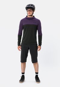 Maglietta long-sleeve nera e viola con cappuccio, abbinata a pantaloni corti neri. Il modello indossa un casco nero e occhiali, mostrando un design sportivo.
