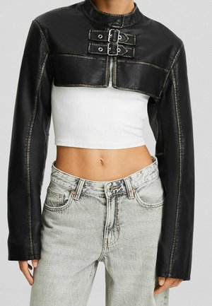 Cropped black leather jacket with front zipper and two buckles, worn over a white ribbed crop top and light gray high-waist jeans.
