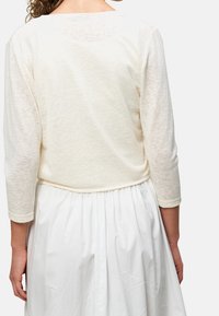 Lehký krémově barevný top s tříčtvrtečními rukávy, s texturovanou látkou a rovnými lemy, doplněný o bílou plisovanou sukni.