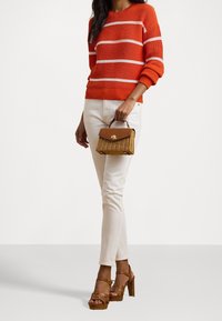 Ljusa orange randiga stickade tröja med långa ärmar, matchad med vita åtsittande byxor och bruna klacksandaler. Liten brun vävd handväska.