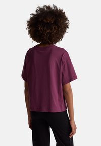 Koszulka z krótkim rękawem, okr�ągłym dekoltem w głębokim burgundowym kolorze, wykonana z bawełny. Posiada luźny krój z bocznymi rozporkami dla większej swobody ruchu.