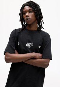 Sort bomulds t-shirt med en løs pasform, prydet med hvid tekst og grafik: "NEW JERSEY THE GARDEN STATE" og et solmotiv på ærmet.