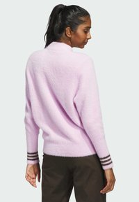Lys pink, fluffy sweater med krave, afslappet pasform og brune stribede detaljer ved manchetterne. Båret med mørke bukser, der fremhæver den bløde tekstur.