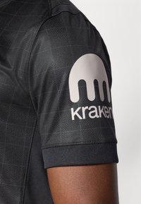 Maglietta atletica nera con superficie testurizzata, con un grande logo grigio chiaro e la scritta "kraken" sulla manica sinistra.
