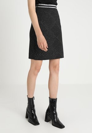 Woman wearing a black textured skirt with silver waistband stripes and black shiny ankle boots with block heels on a white background.