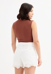 Top marrón sin mangas combinado con pantalones cortos blancos de talle alto que presentan patrones de corte intrincados y un dobladillo en forma de ondas. Textura suave en general.
