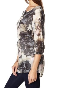 Blusa leggera e trasparente con un motivo floreale in camuffamento nei toni del grigio, beige e rosa pallido. Presenta maniche 3/4 e una vita con coulisse.