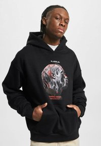 Sudadera negra con capucha que presenta un gráfico de una cara estilizada en rojo y blanco. Tejido suave, bolsillo tipo canguro en el frente, puños y dobladillo acanalados.