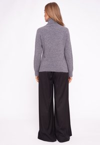 Szary golf z miękkiego materiału w połączeniu z czarnymi spodniami o szerokich nogawkach, prezentującymi luźny krój i prosty design.