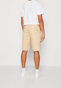 Khaki shorts i en bomullsblandning, med gylf, två bakfickor och en logotags på höger ficka. Bärs med en vit T-shirt och sneakers.