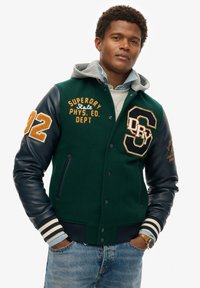 Groene wollen en marine leren varsityjack met oranje accenten, voorzien van geborduurd logo, gestreepte manchetten en een grijze capuchonvoering.