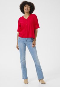 Camicia rossa a maniche corte con colletto frill, abbinata a jeans azzurri a palazzo e scarpe beige con tacco. Design semplice.