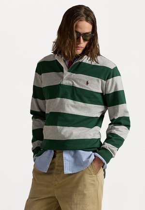 Groen en grijs gestreepte rugbyshirt met een kraag en een logo op de borst, gedragen over een lichtblauw overhemd met knopen en khaki broek.