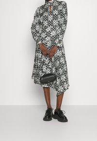 Černobílé vzorované šaty s dlouhými rukávy, vysokým límcem a výřezem ve tvaru klíče; zkombinované s černými botami a malou kabelkou.