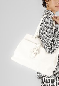 Borsa a mano in pelle bianca con dettaglio intrecciato e hardware dorato, dotata di doppi manici superiori e una forma morbida e strutturata.