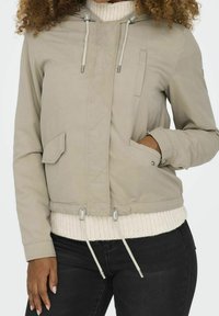 Beige lightweight jacket with a hood, featuring elastic cuffs, drawstring hem, and side pockets. Textured knit collar adds detail.