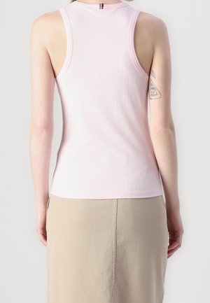 Kobieta ubrana w jasnoróżowy prążkowany tank top i beżową spódnicę, pokazana od tyłu, z małym tatuażem na prawym ramieniu.