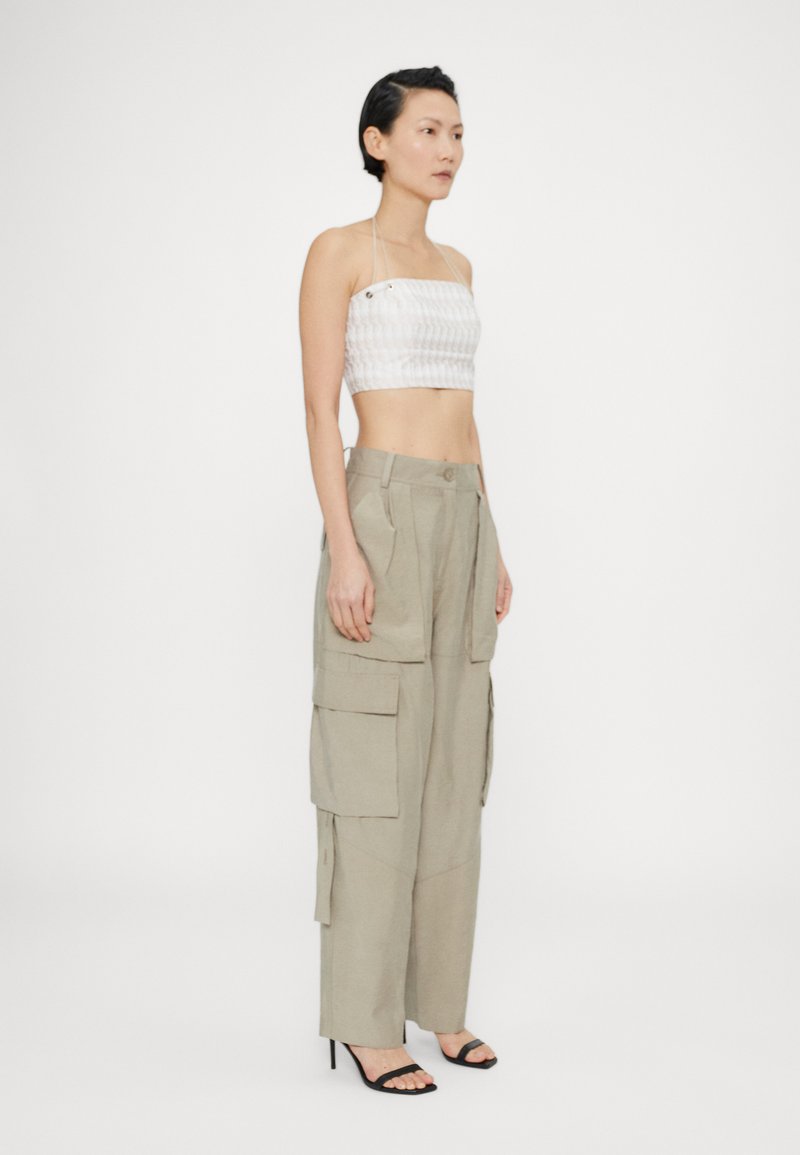 Top corto bianco senza spalline con motivo testurizzato, abbinato a pantaloni cargo beige a vita alta con ampie tasche laterali e vestibilità rilassata.