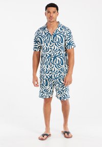 Korte mouwen Hawaiiaans overhemd en bijpassende shorts in marineblauw en crèmewit met een bladerenpatroon, gemaakt van lichtgewicht stof. Voorzien van knoopsluiting.