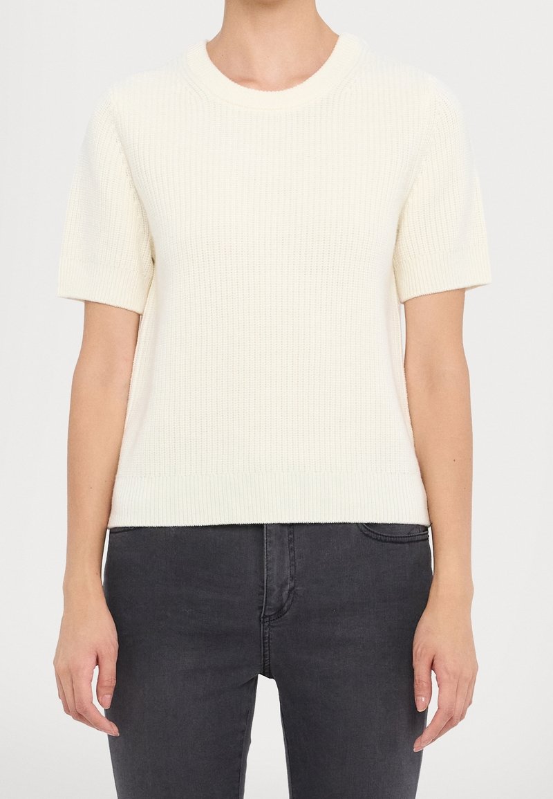 Pull en tricot côtelé à manches courtes de couleur crème avec un col rond, présentant un motif texturé et un ourlet droit à la taille.