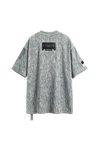 Camiseta gris de manga corta con un patrón texturizado único, cuello ancho y etiqueta rectangular negra cosida en la parte posterior.