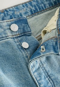 Vaaleansiniset farkut, joissa on haalistunut pinta. Varustettu hopeisilla nappeilla ja näkyvillä ompeleilla, vyötärönauhassa on merkintä "FLARE FIT".