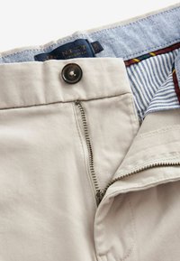 Pantalones rectos beige con cremallera, cierre de botón y un interior de cintura de chambray con acentos de tela a rayas y de colores.