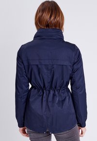 Giubbotto leggero navy con colletto alto, vita cinchata e texture morbida. Presenta una yoke posteriore e dettagli con bottoni a pressione sull'orlo.