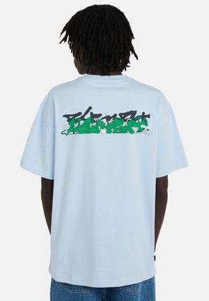 T-shirt bleu clair à manches courtes avec un imprimé coloré de style graffiti au dos. Coupe ample avec une texture lisse et un col rond.