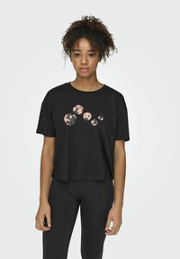 Camiseta corta negra con un diseño gráfico que presenta círculos claros y oscuros. La tela tiene una textura suave y el corte es holgado.